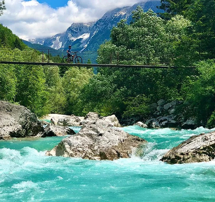 Cyclist crossing a suspension footbridge over the emerald Soča river