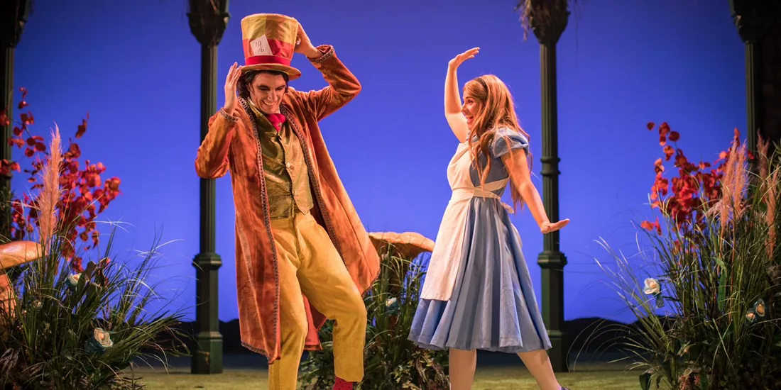 The Mad Hatter and Alice dance together on stage in a vibrant, colourful production number