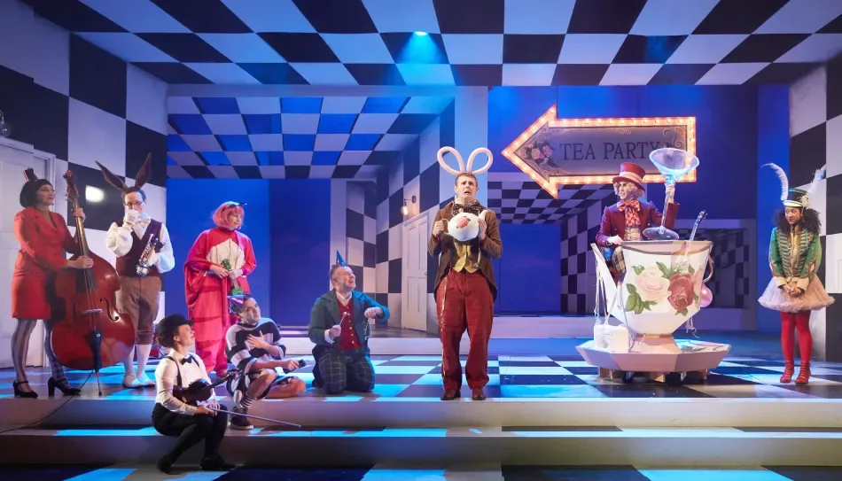 A vibrant musical tea party scene from an Alice in Wonderland stage production, featuring live musicians and colourful characters