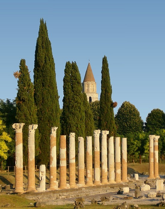 The Roman forum colonnade at Aquileia with the Basilica bell tower rising behind cypress trees