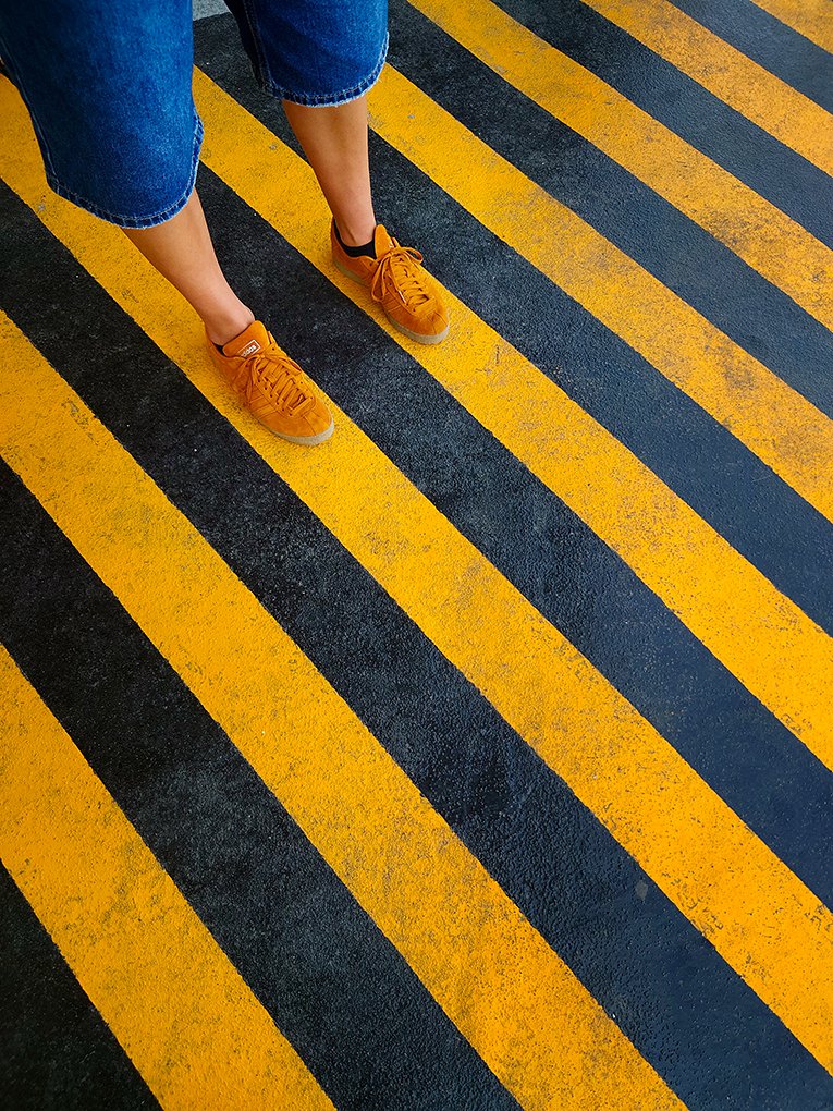 Yellow sneakers standing on a black-and-yellow striped road surface — photograph from FOTONI