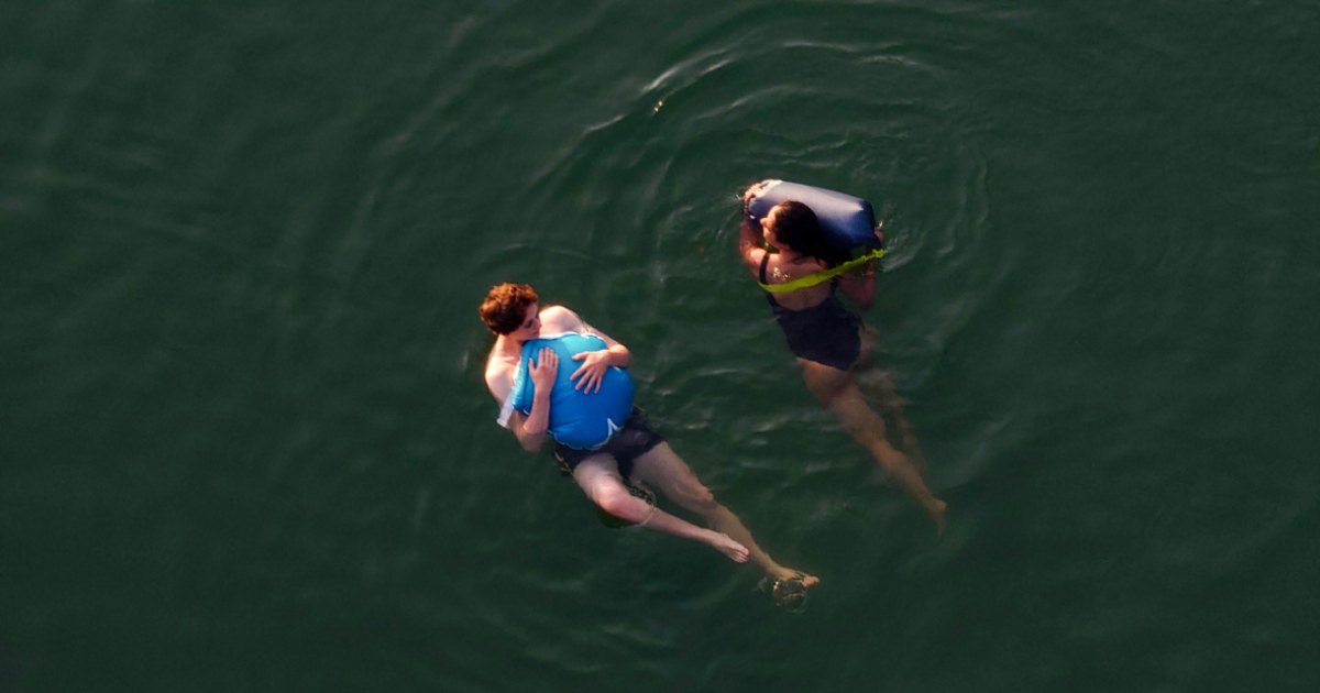 Aerial view of two swimmers floating on dark green water — photograph from FOTONI
