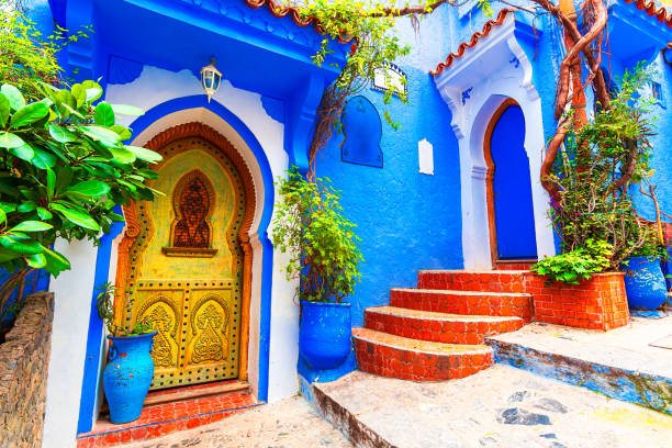 A golden ornate doorway set into a deep blue wall with red steps in Chefchaouen
