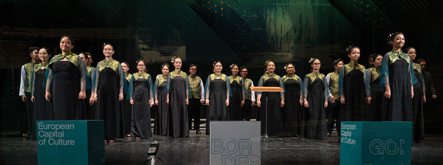 International choir performing at the Seghizzi Competition with GO! 2025 branding