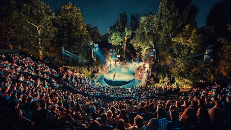 A packed open-air theatre glowing beneath a starry night sky