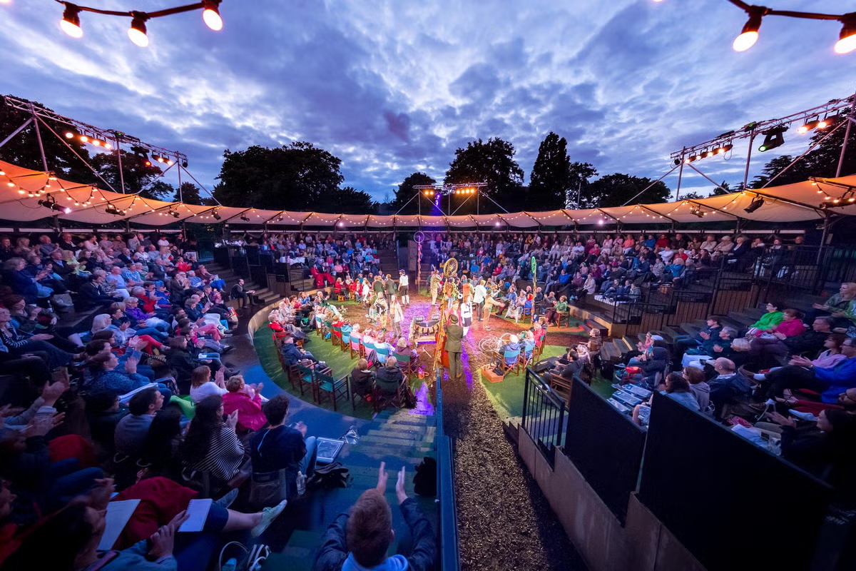 An amphitheater audience at dusk under strings of lights